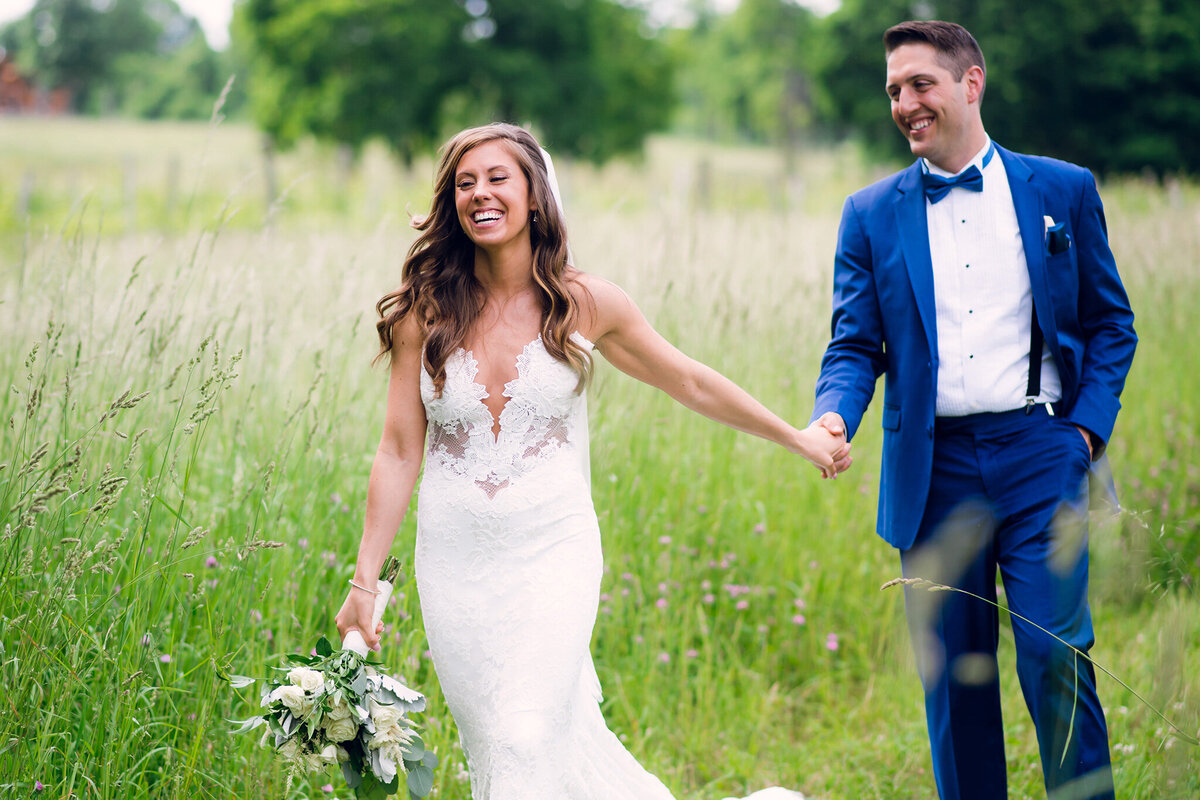 A bride and groom walking through a field of tall grass.
