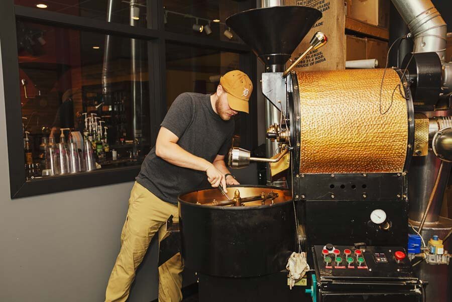 A man roasting coffee beans using an industrial coffee roaster in a café setting.