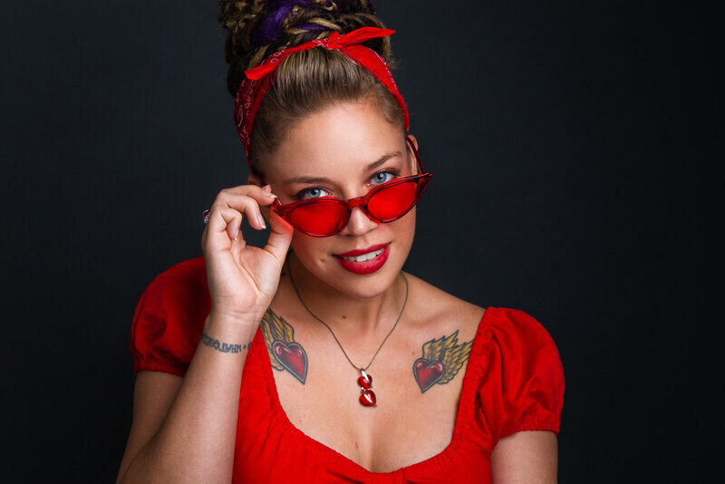 woman in bright red top and head bandana pulling down her bright red glasses