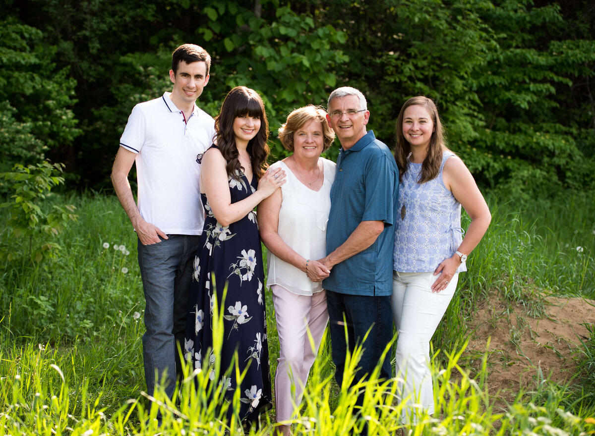 a photo of mom, dad and their adult children taken in a grassy field during their family photography session in Ottawa