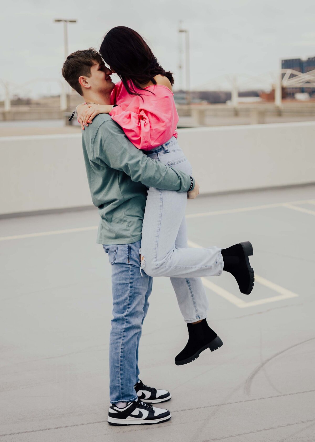 Maddie Rae Photography couple on the top of a parking garage. they are face to face and he has picked her up. they are giving eskimo kisses