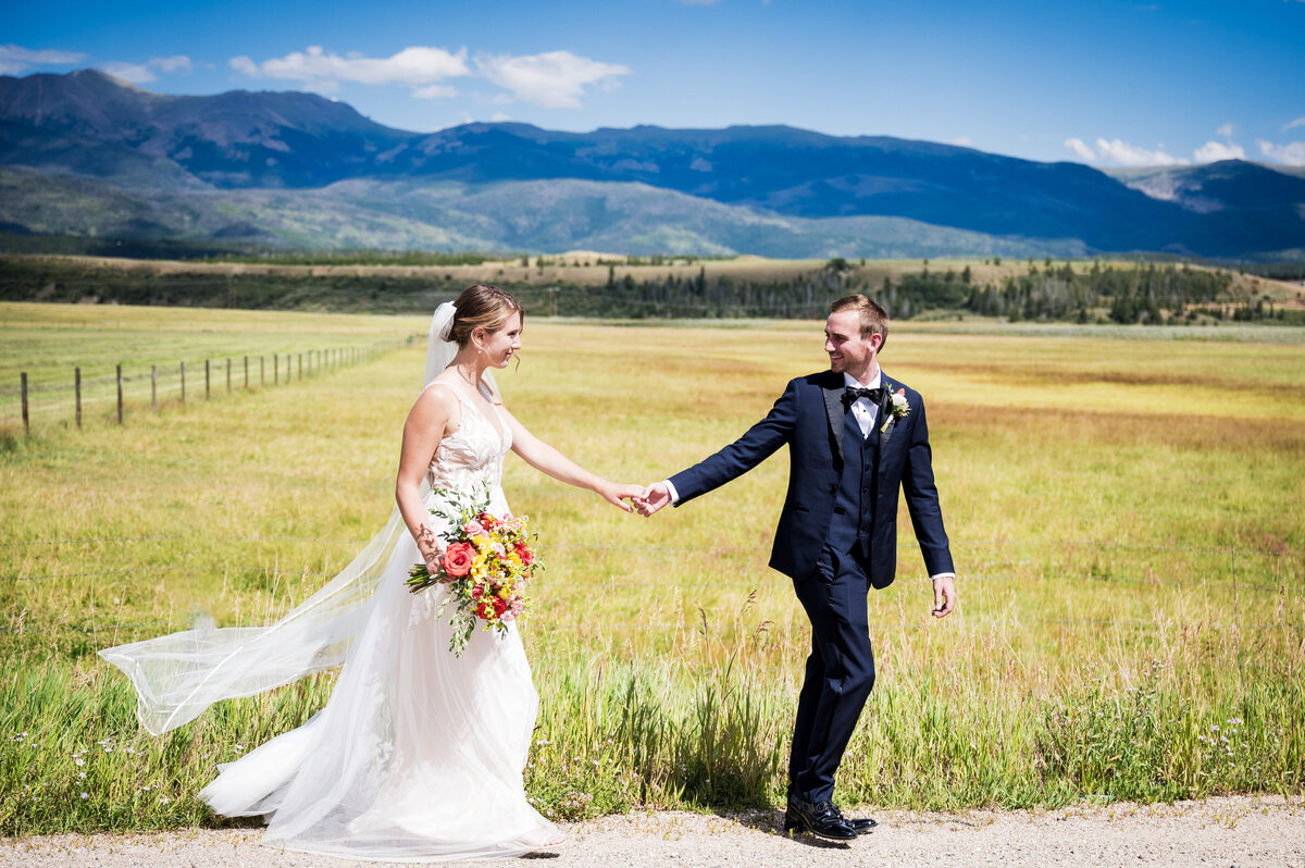 A groom takes his bride's hand and leads her with scenic Colorado landscape in the background.