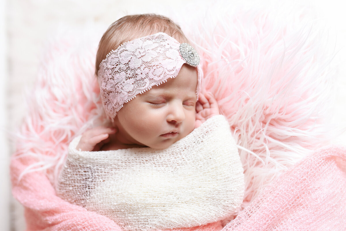 Beautiful Mississippi newborn photography: newborn girl wrapped in ivory with rhinestone headband in a pink flokati bed