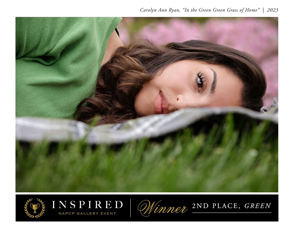 Portrait of a young lady in a green cardigan with dark hair laying on a blanket and looking at the camera. The blanket blocks the right side of her face with the unique angle and pose.  Words on the title say "Carolyn Ann Ryan, In the Green Green Grass of Home | 2023. The bottom says "Inspired NAPCP Gallery Event  Winner, 2nd place, Green"