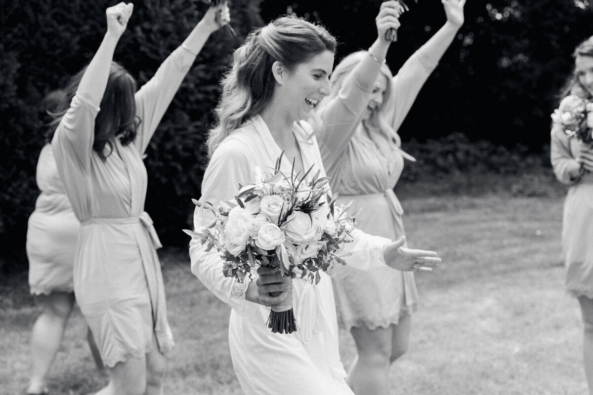 bride smiling and holding flower bouquet running with bridesmaids with raising hands