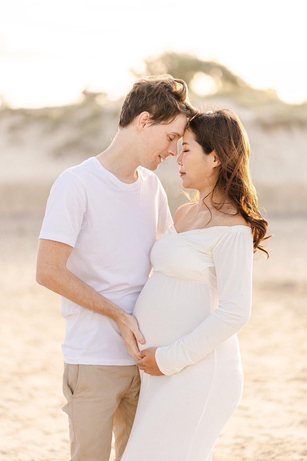 Intimate couple wearing white on the beach having maternity photos taken in Gold Coast QLD