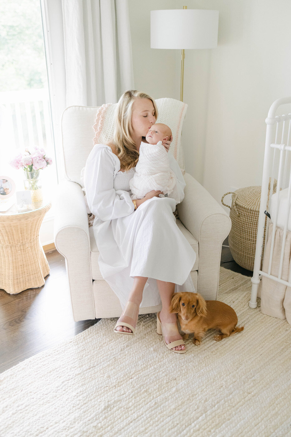 Mom holding and kissing newborn baby with dog curled up at her feet