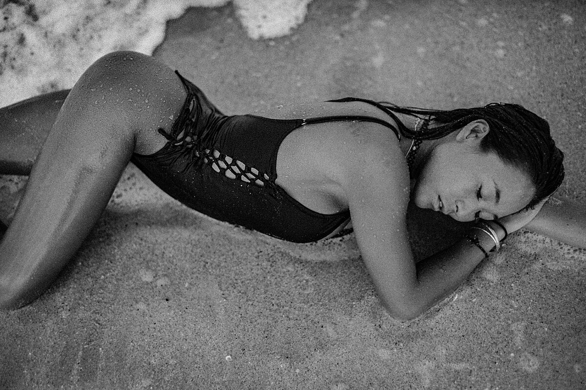 black and white photo of a woman resting her head in the sand as the ocean splashes her back on a Maui beach