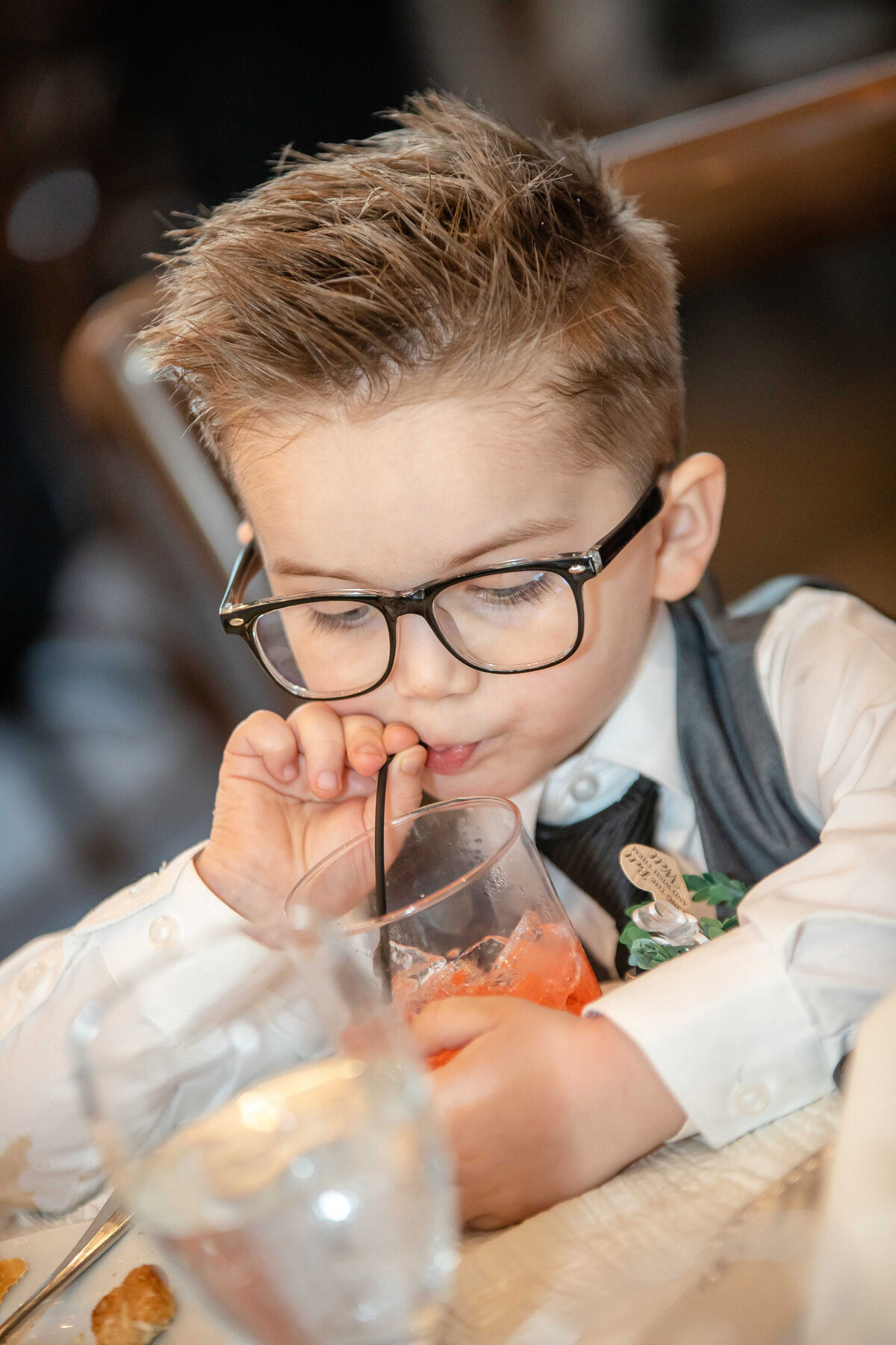 cute little boy in glasses sips from straw at wedding