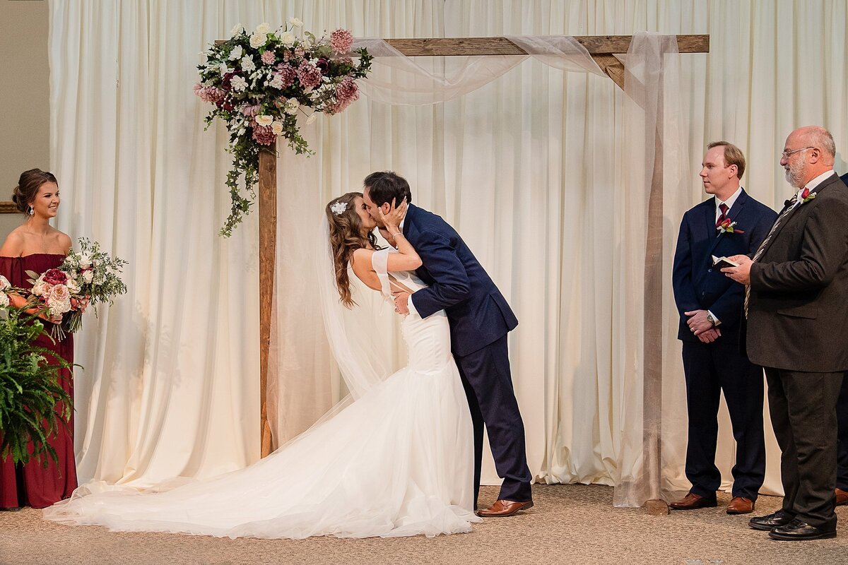 bride and groom first kiss in front of sheer curtain under wooden arch
