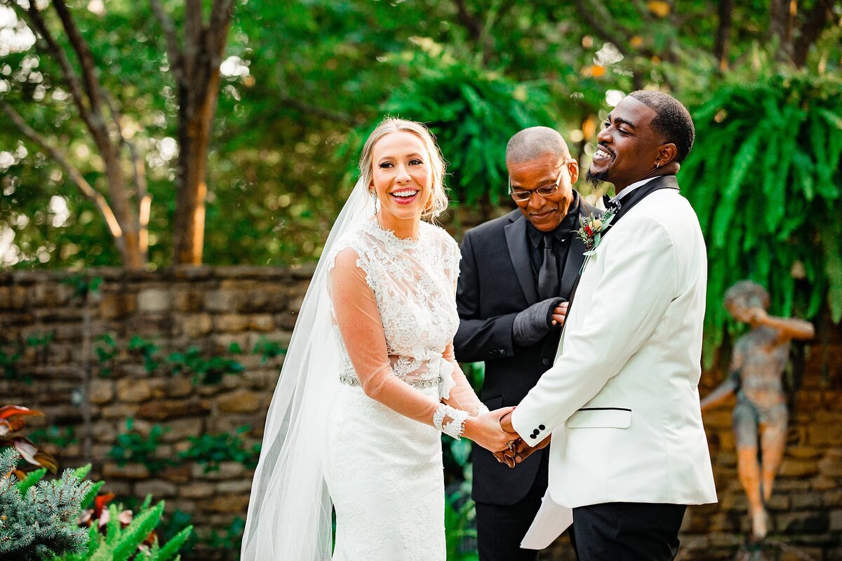 Bride and groom holding hands in a courtyard exchanging vows and laughing