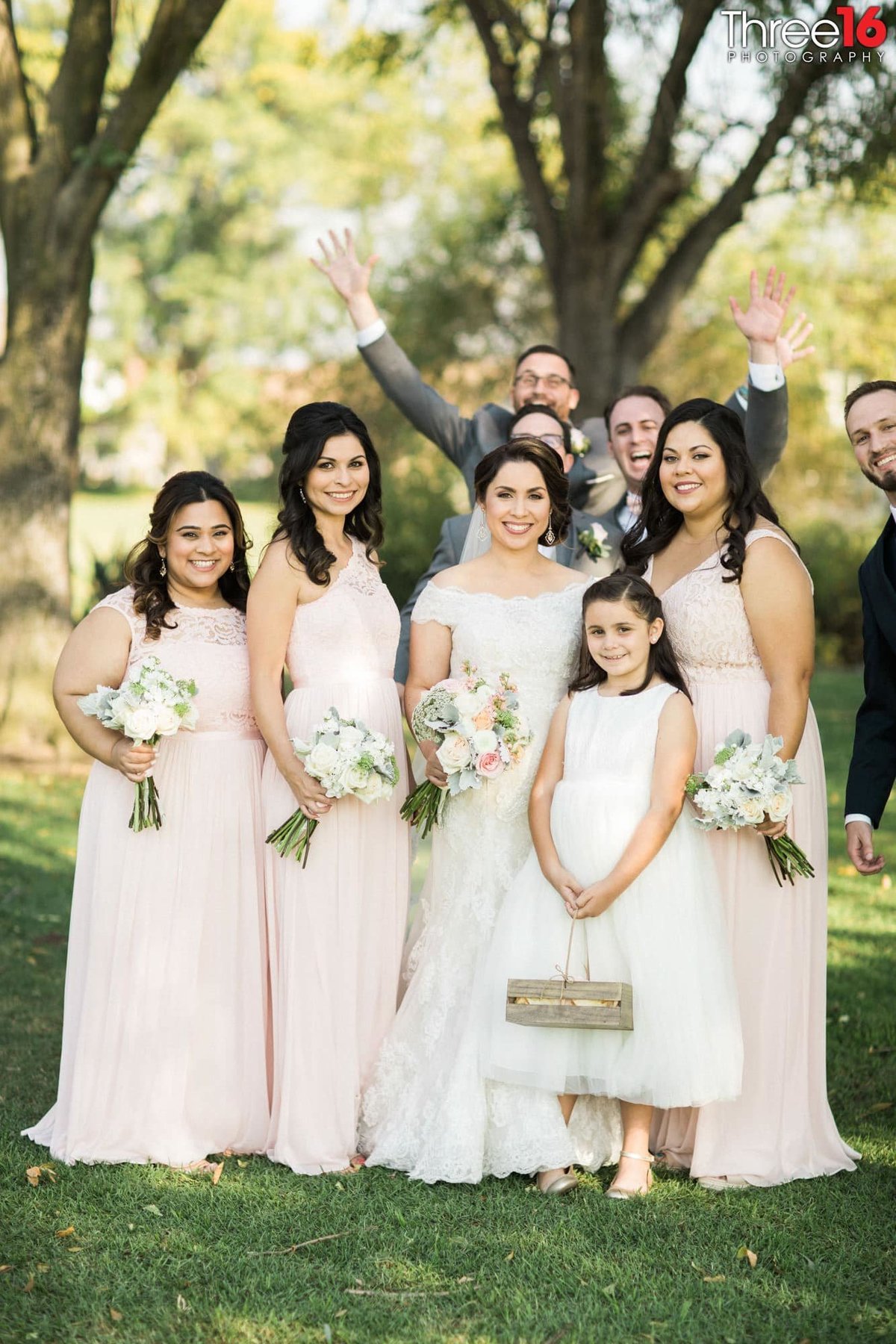 Groomsmen photobomb Bride as she poses with her Bridesmaids and Flower Girl