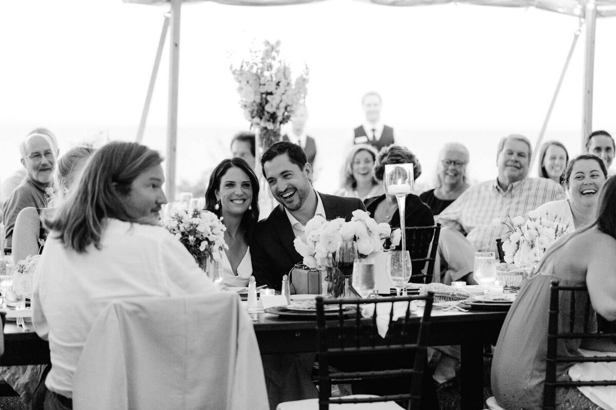 Black and white photo of the bride and the groom, together with guests, seated at dining tables in Cape Cod Summer Tent, MA.