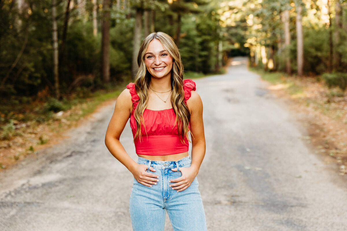 beautiful girl in a red crop top and jeans smiling with her thumbs in her belt loops