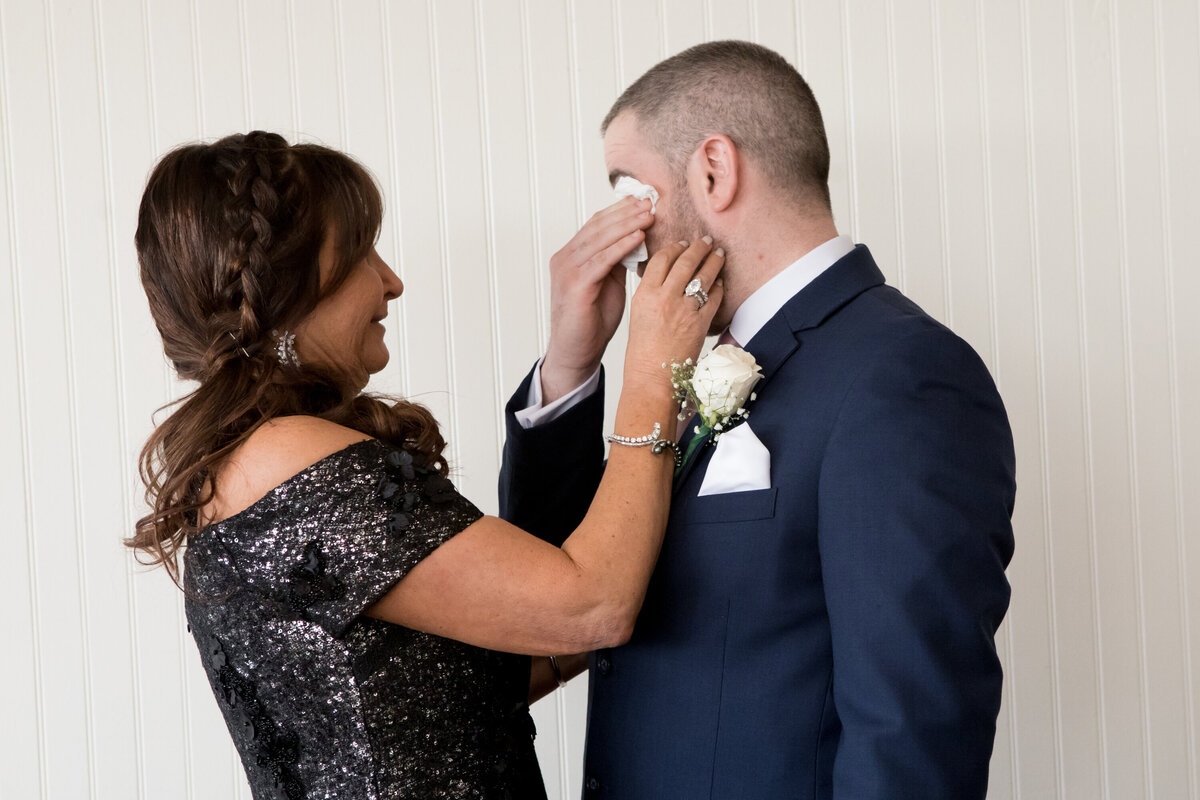 Mother of the groom in dequine dark grey dress wipes away her adult son's tears the Garrison wedding photographer Milestone Images