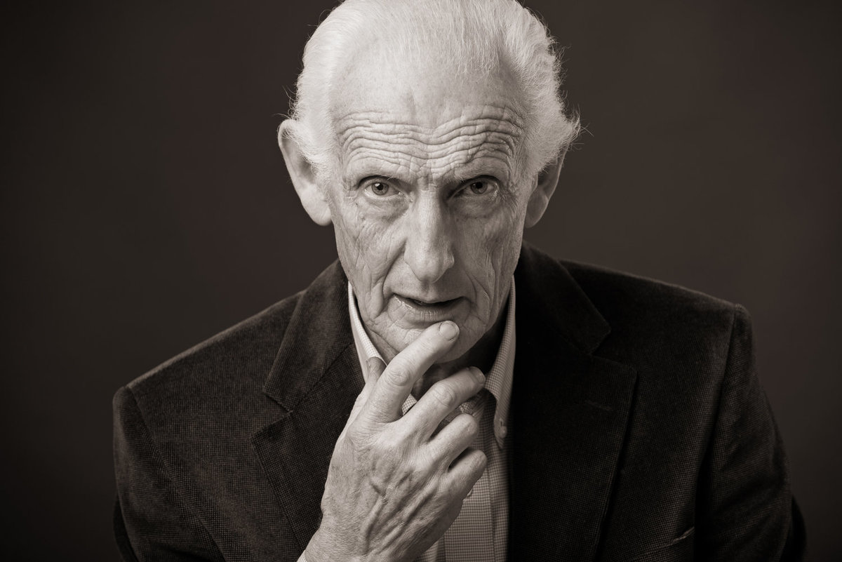 Black & white portrait of an elderly man looking serious with hand to mouth