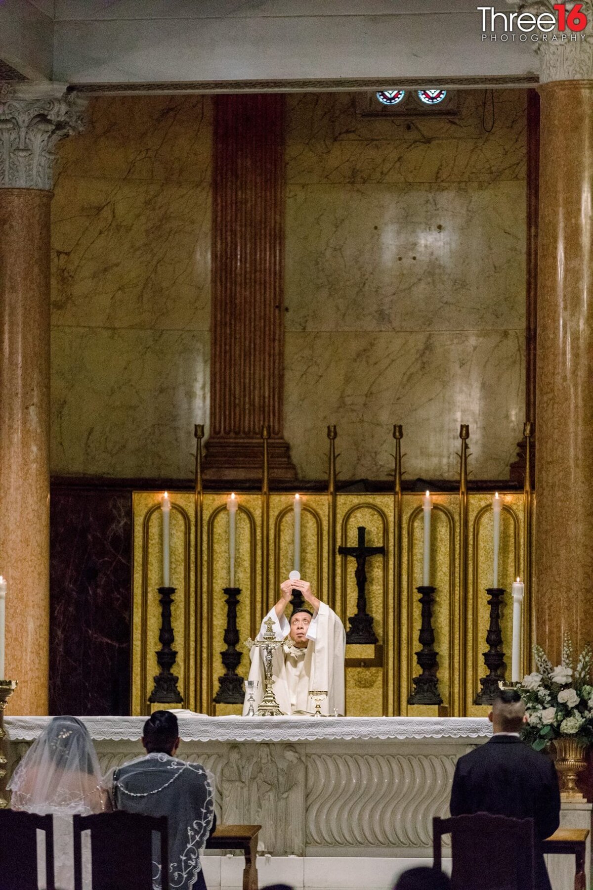 Priest performs a Catholic wedding ceremony as the Bride and Groom sit in chairs facing the altar