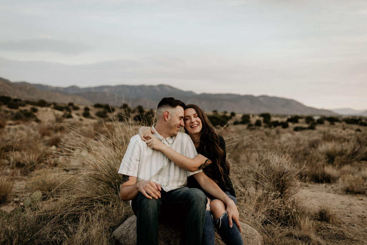engaged couple sitting on a rock smiling in the desert