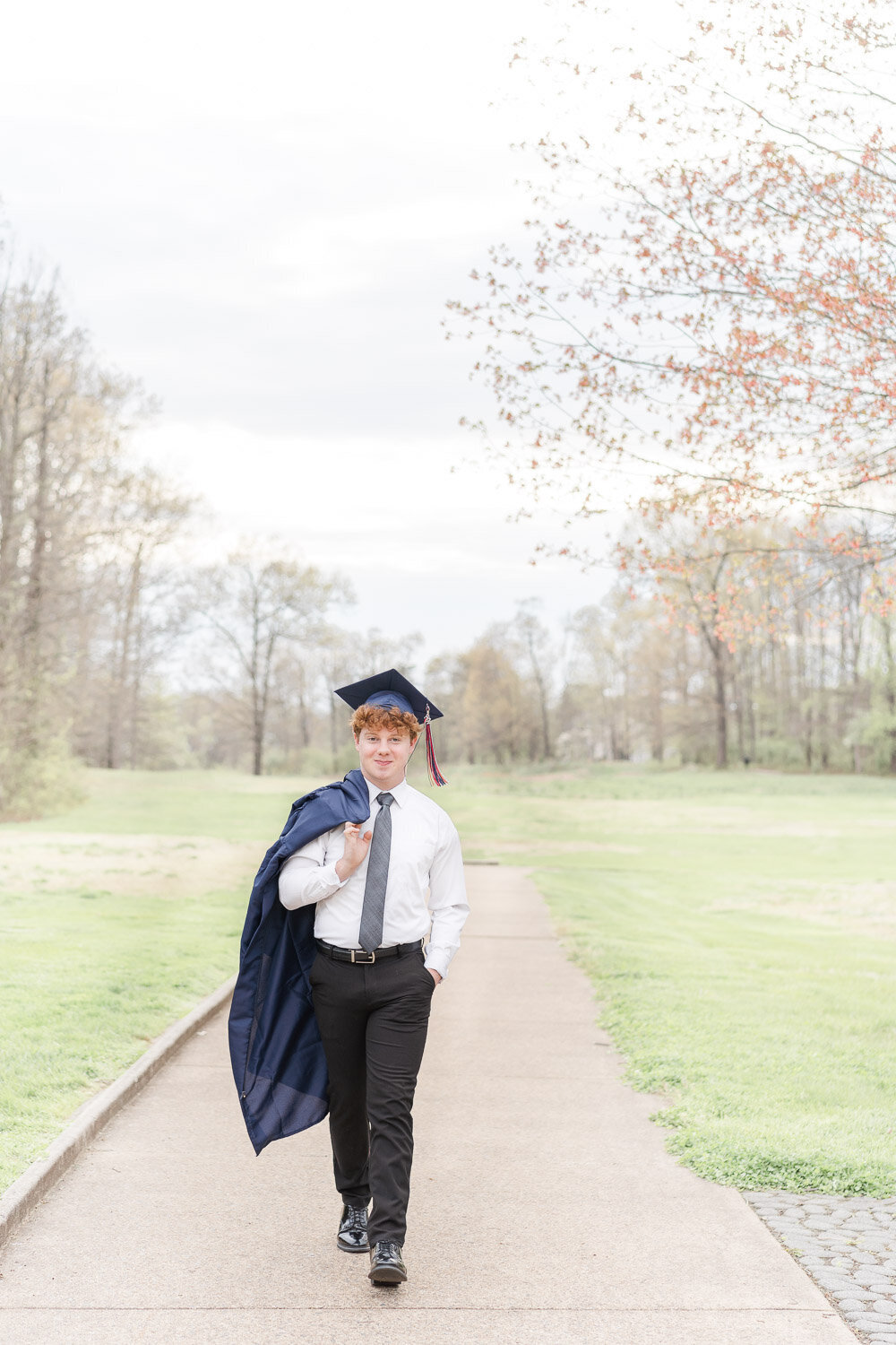 boy wearing graduation cap holding his gown while walking during his Manassas, VA senior photos