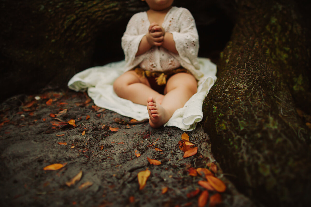 a toddler laying between a tree wearing a boho tassel velvet romper