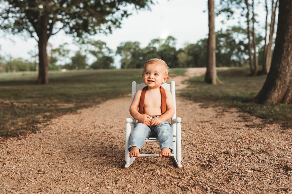 wide angle of a baby boy wearing jeans, rocking on white rocking chair.