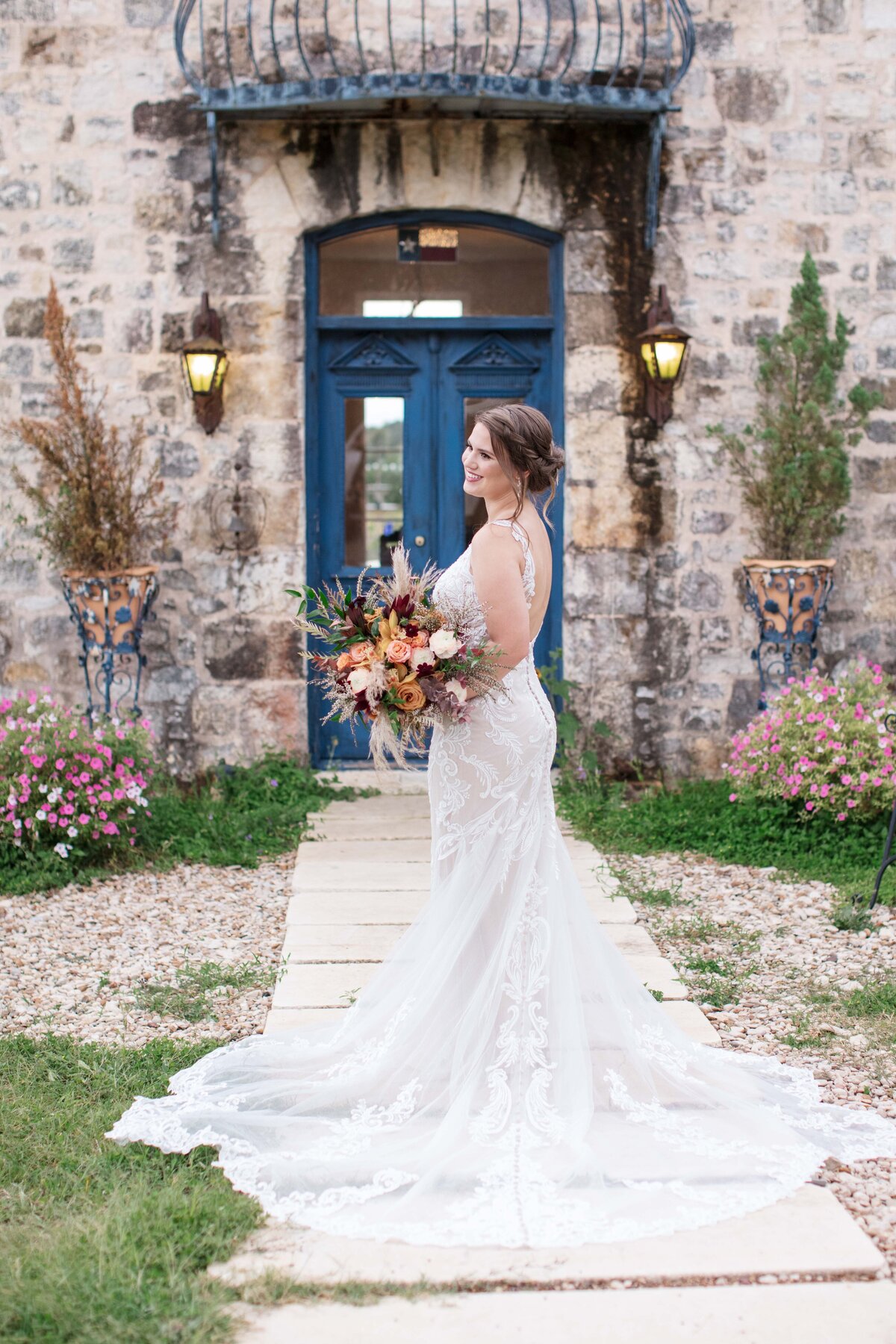 blue door of French style wedding venue with bride holding bouquet and train draping steps by Firefly Photography