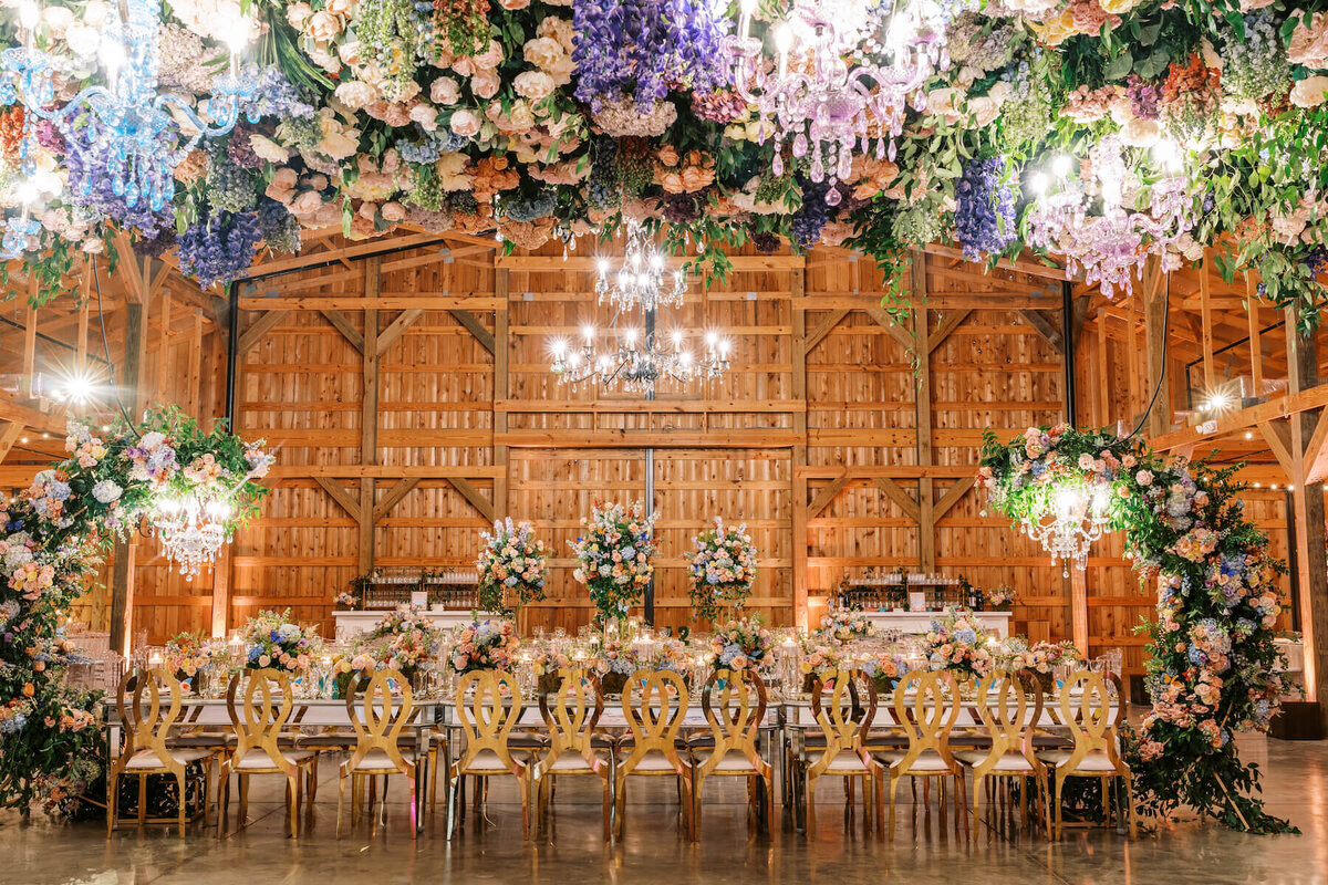 Pastel flowers hanging over dance floor and surrounding head table with chandeliers at wedding reception.