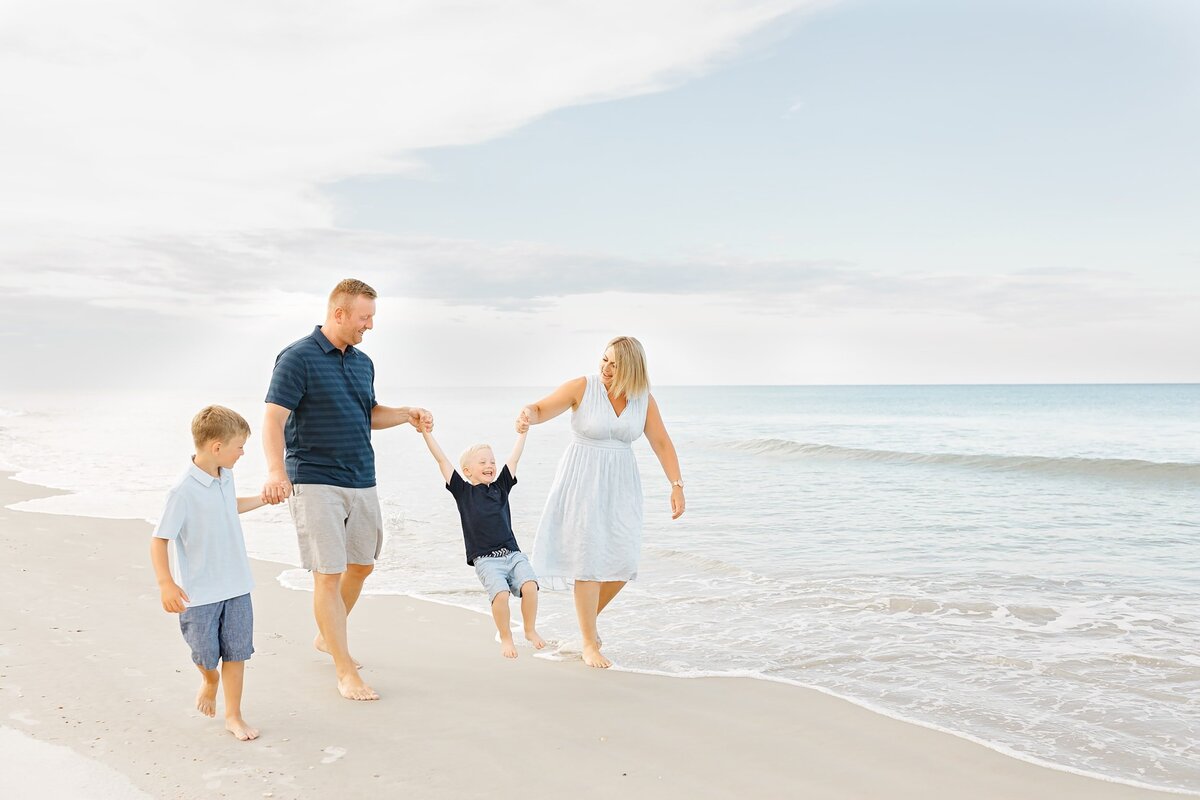 Family of 4 holding hands walking along the beach