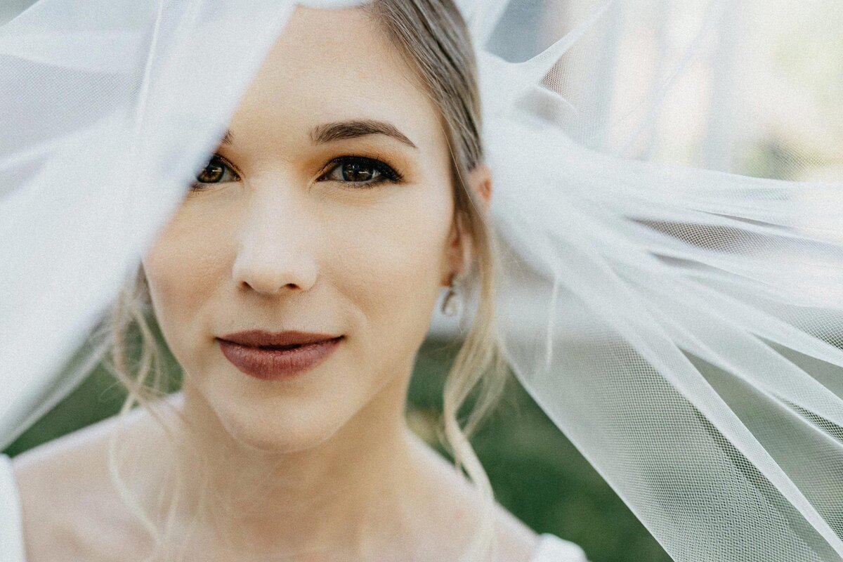 A close-up of a bride's face veiled in tulle, with a serene and content expression