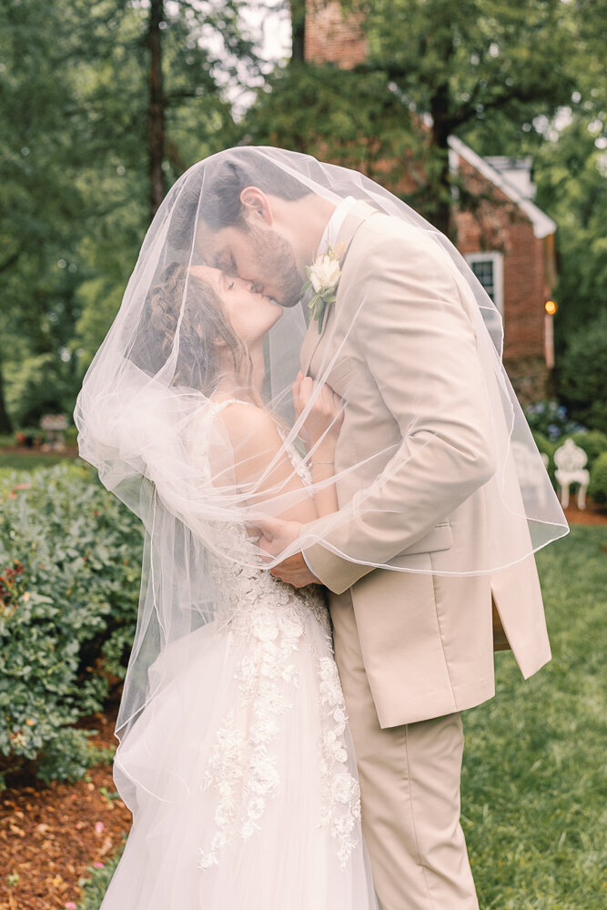 A couple kisses under a wedding veil during their Catholic wedding.