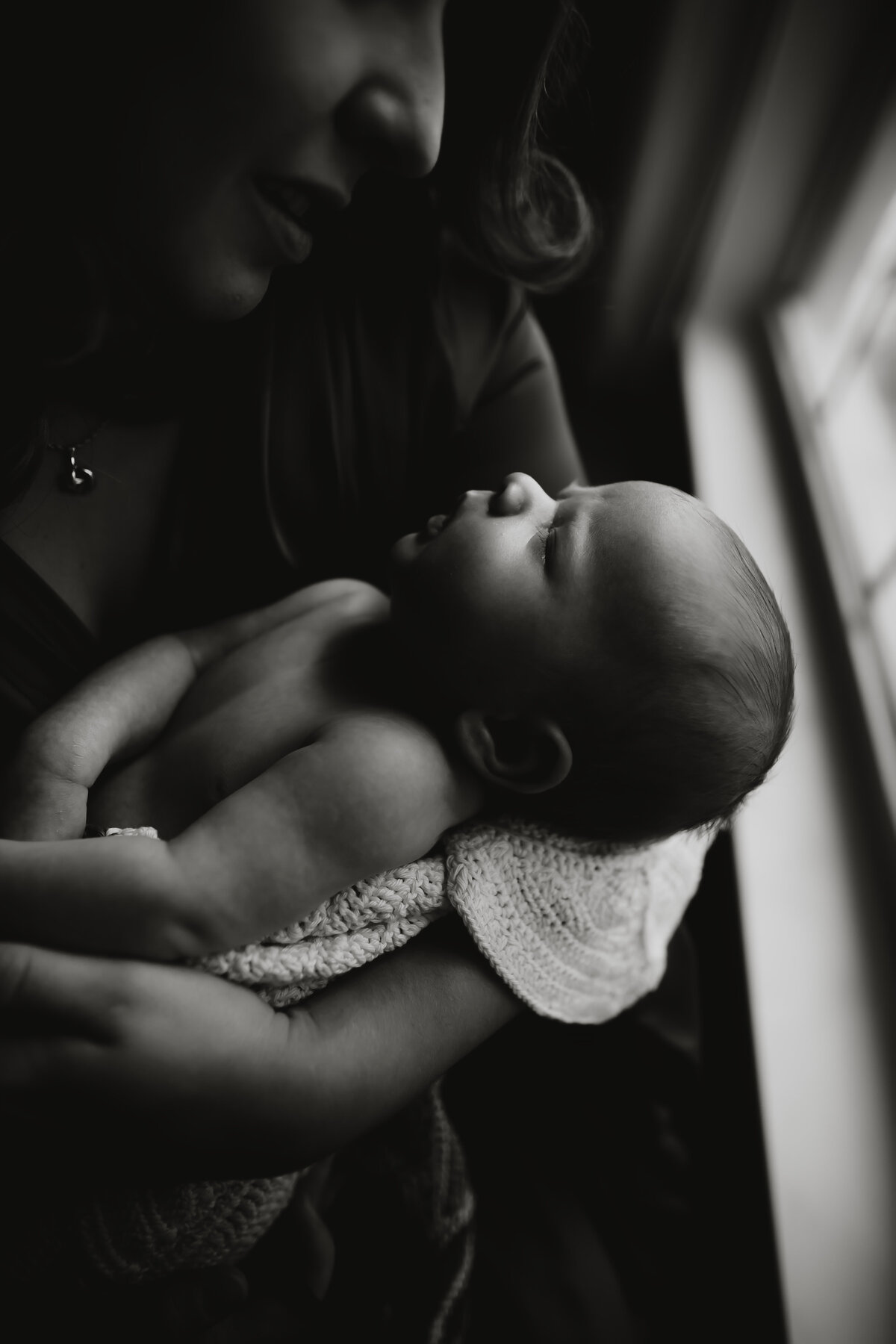 beautiful moody and emotional portrait of a mom holding her rainbow baby in front of a window during a newborn photo shoot at home