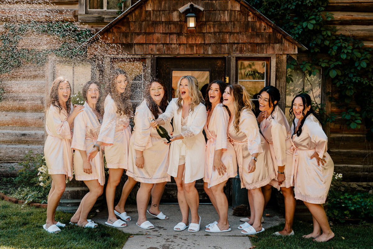 While in their getting ready gowns, the bride and bridesmaids shake and pop a bottle of champagne.