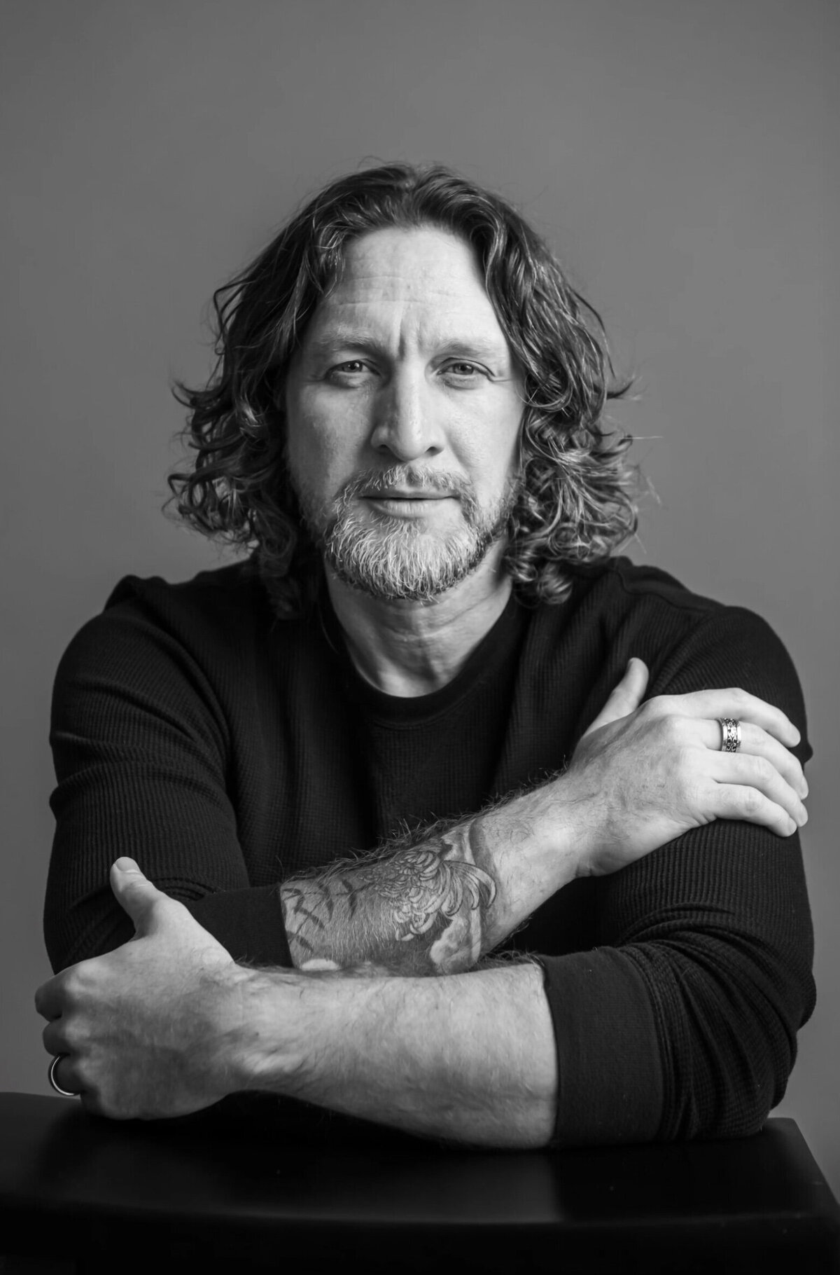 Man with curly hair and tattoos, posing for a headshot with his arms crossed