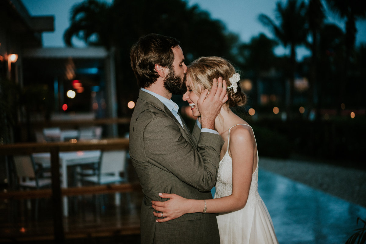Groom holds bride's face and kisses her forehead in the rain on wedding night at Sandpiper Bay Club Med