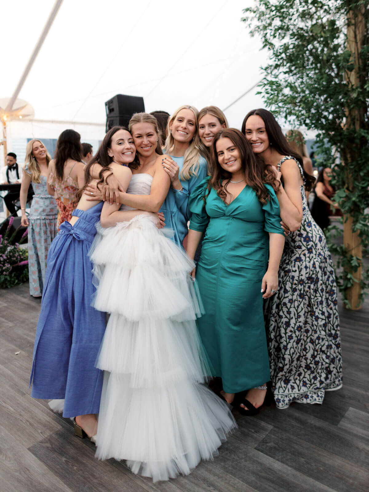 The bride is hugging a bridesmaid, along with other bridesmaids at the wedding reception at The Ausable Club, NY. Image by Jenny Fu Studio