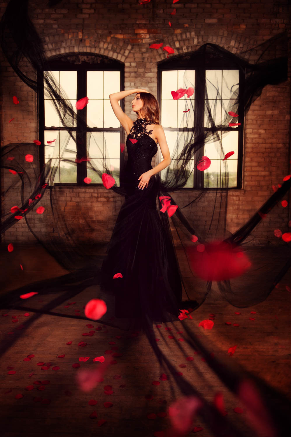senior girl in formal black dress with rose petals in a studio