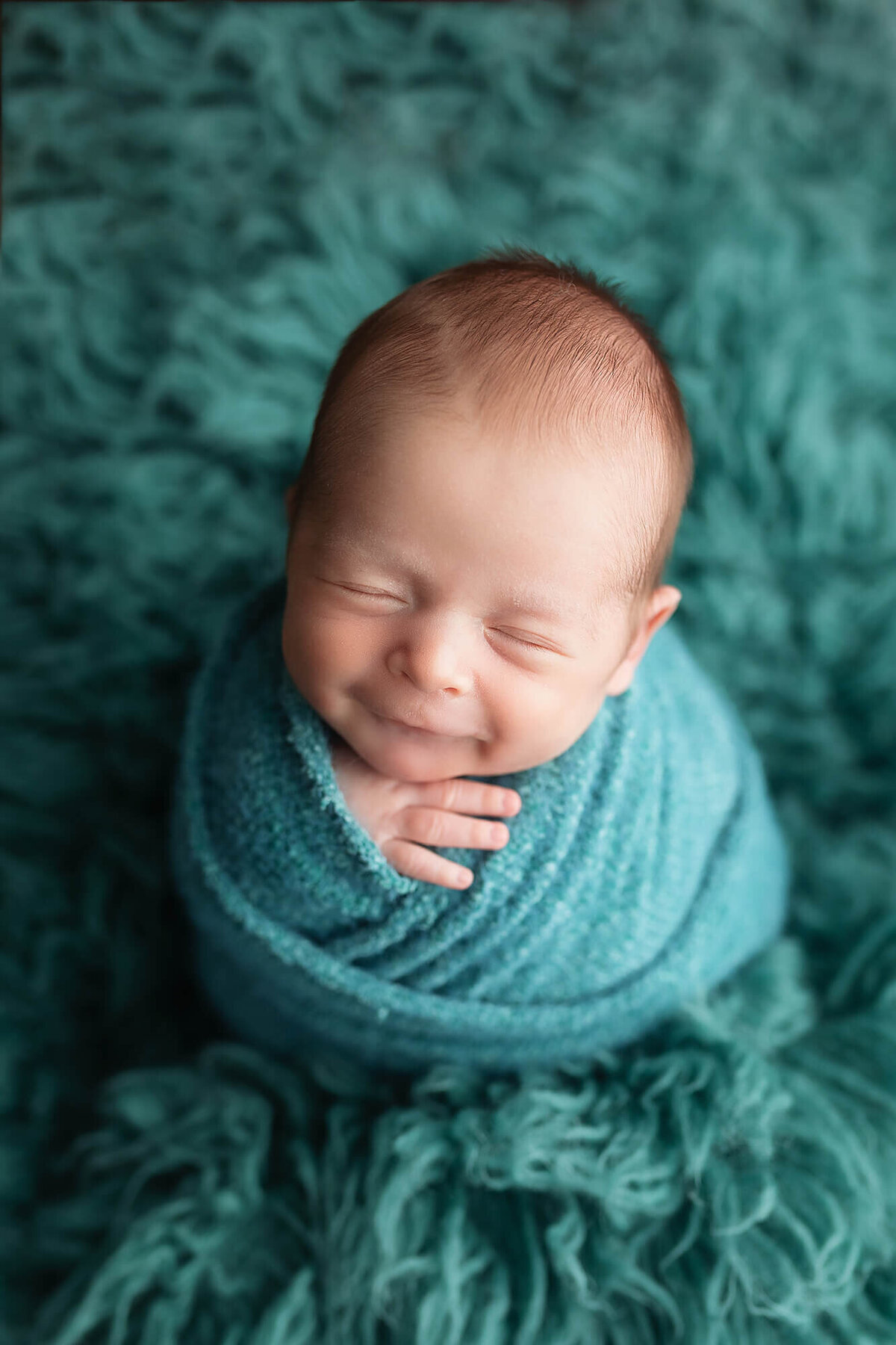 Smiling newborn wrapped in teal blue.