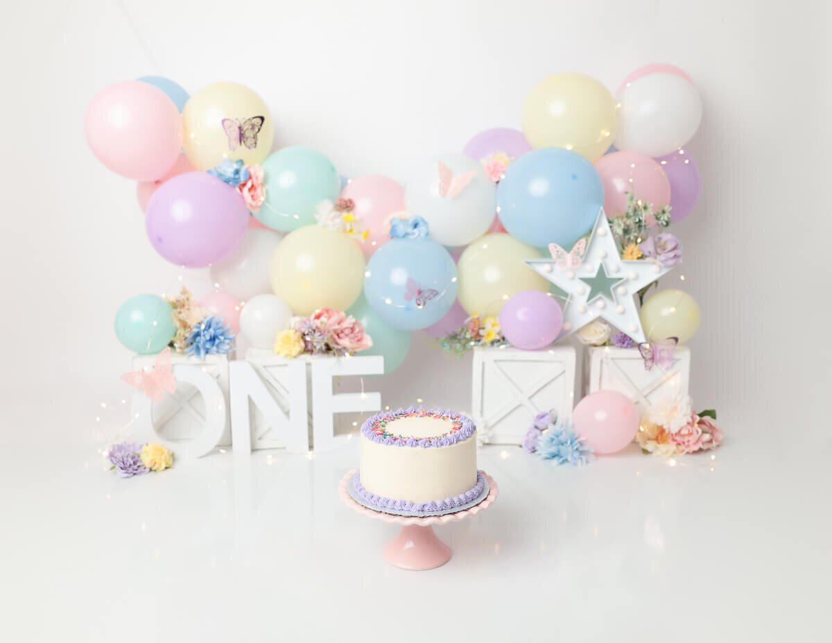 A decorated cake surrounded by pastel balloons with a baby preparing to smash it in Rochester, NY.