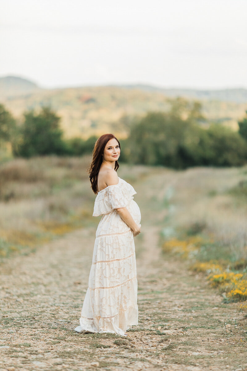 Expecting mom with red hair and white dress on a hillside with small yellow flowers