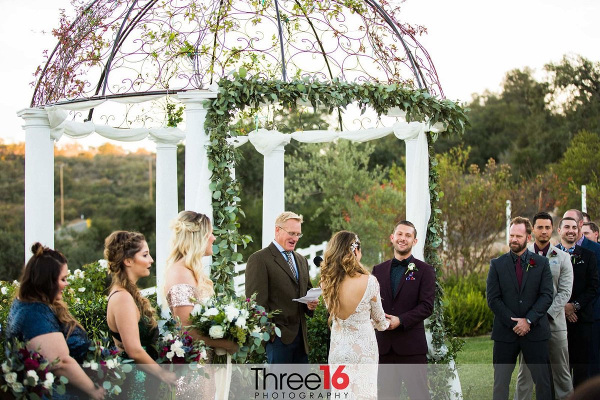 Bride and Groom smile during their outdoor wedding ceremony as the officiant speaks at the Forever & Always Farm wedding venue