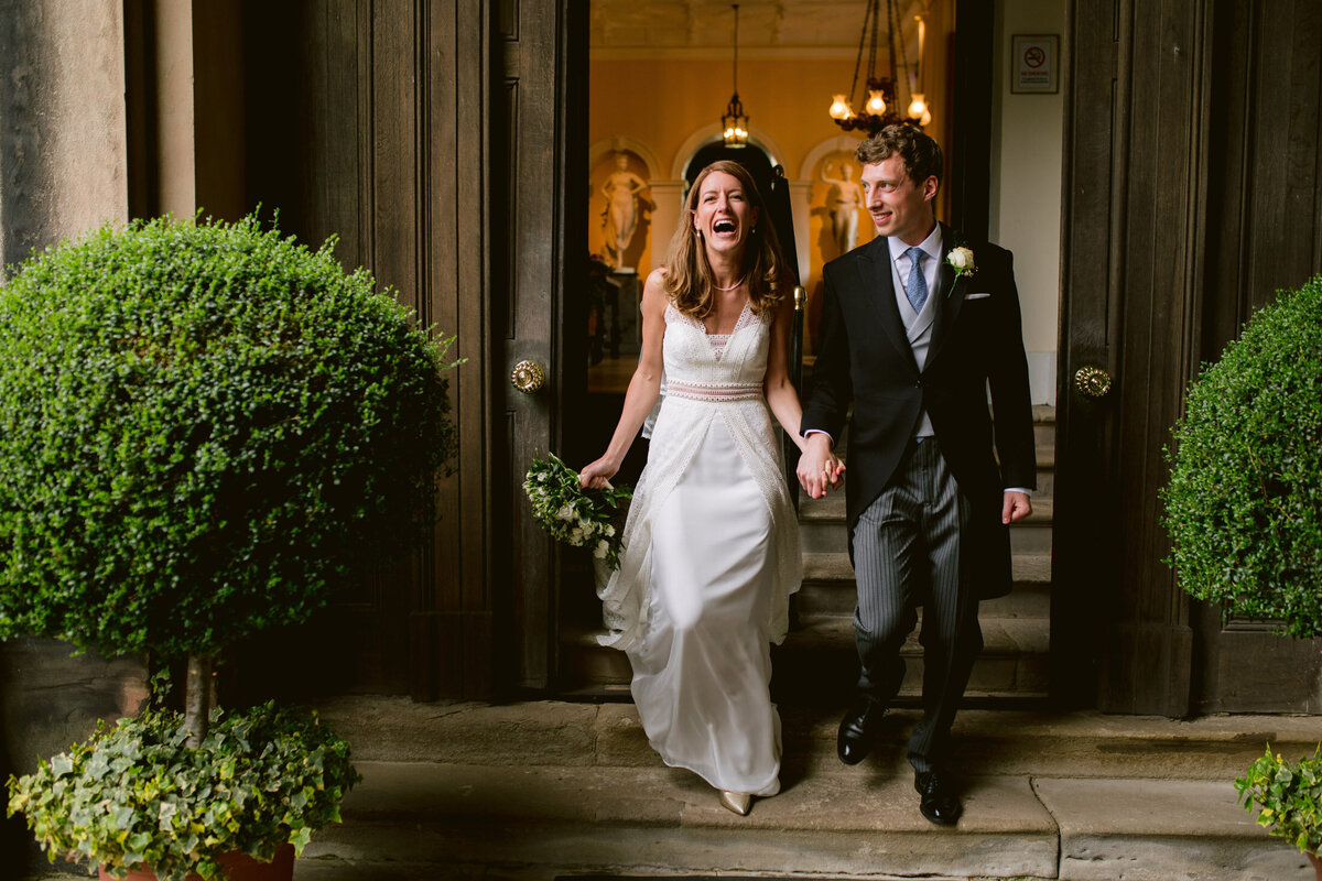 natural wedding photo of bride and groom laughing on the steps of capesthorne hall