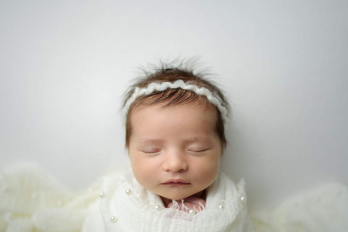 Newborn girl on white with headband in Jacksonville, FL.