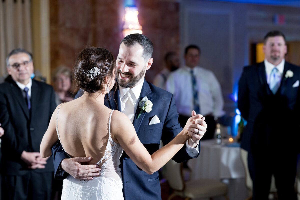 Groom in blue suit smiles at bride with brown hair as they dance in a blue-lit ballroom Hudson Valley New York wedding photographer Milestone Images