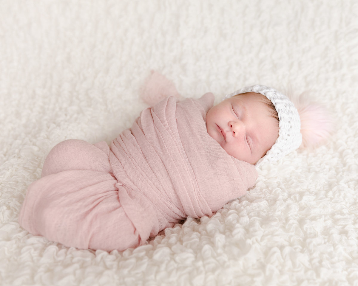 newborn baby swaddled in pink blanket on a white blanket