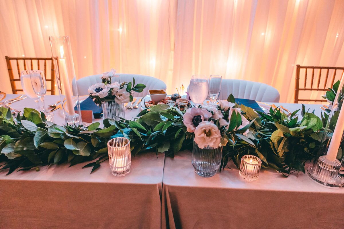 Elegant Iowa wedding reception table decorated with white flowers, green leaves, and candles, with warm lighting in the background.