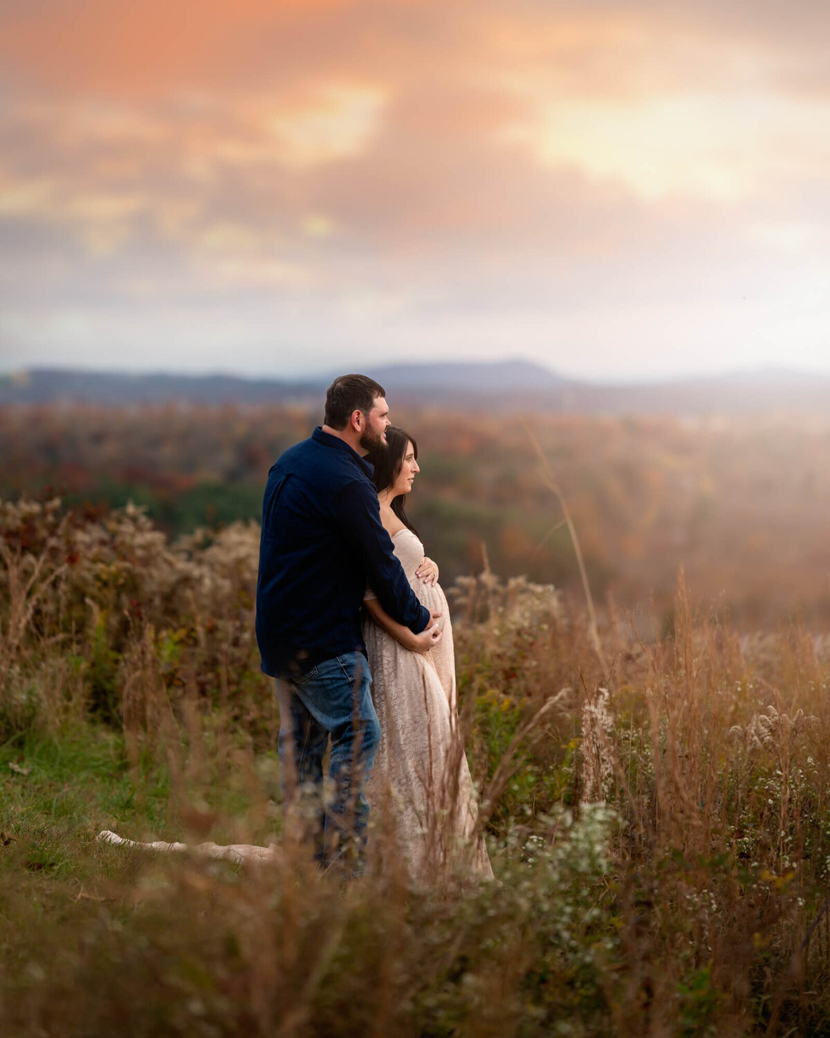 An expecting couple embraces as the dreamy light from a sunset envelopes them