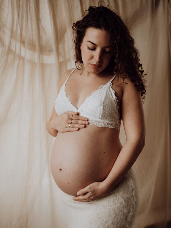 Mama kijkt liefdevol naar haar zwangere buik tijdens haar zwangerschapsshoot te Beveren.