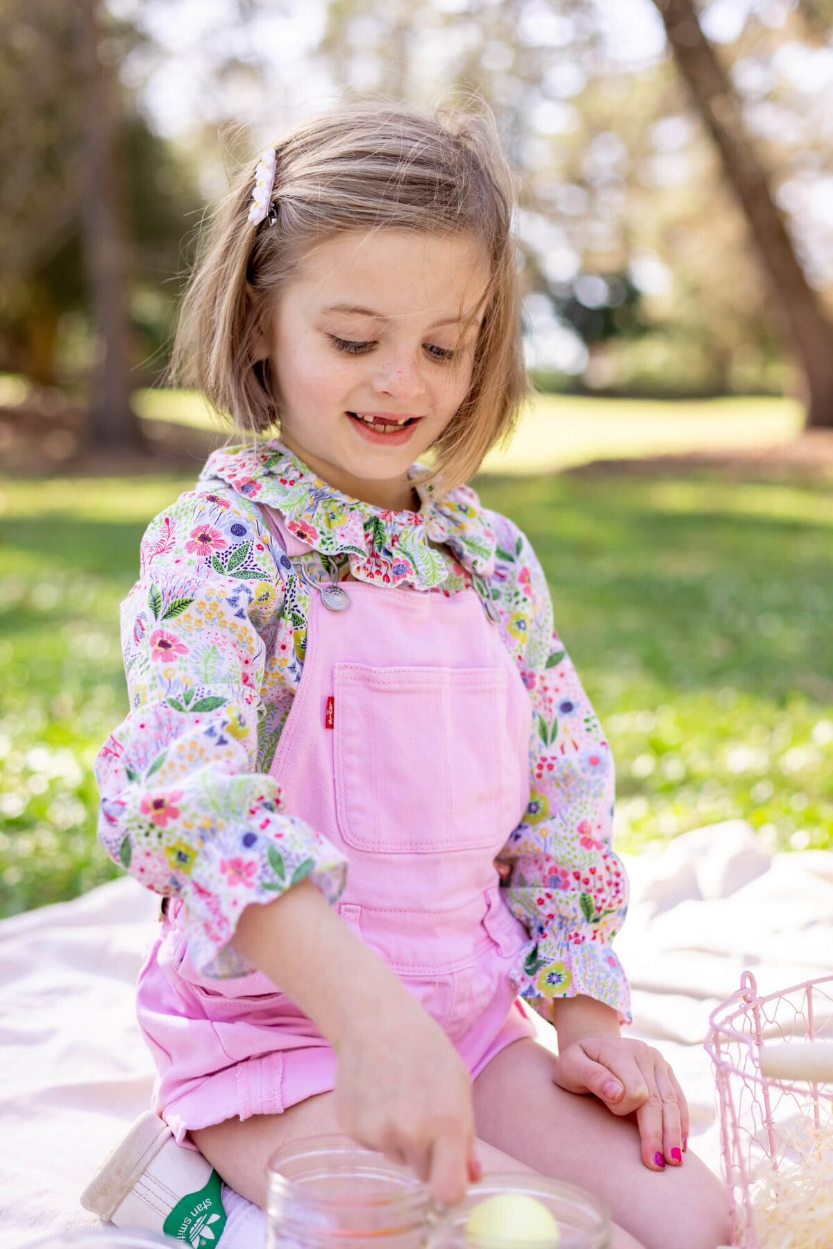Little girl with blonde bob dyes Easter eggs wearing pink overalls