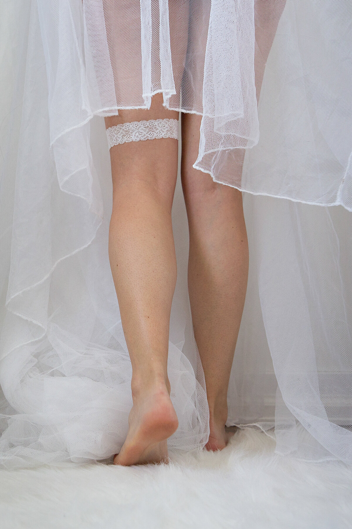 Bright and airy sexy shot of bare legs with garter and veil