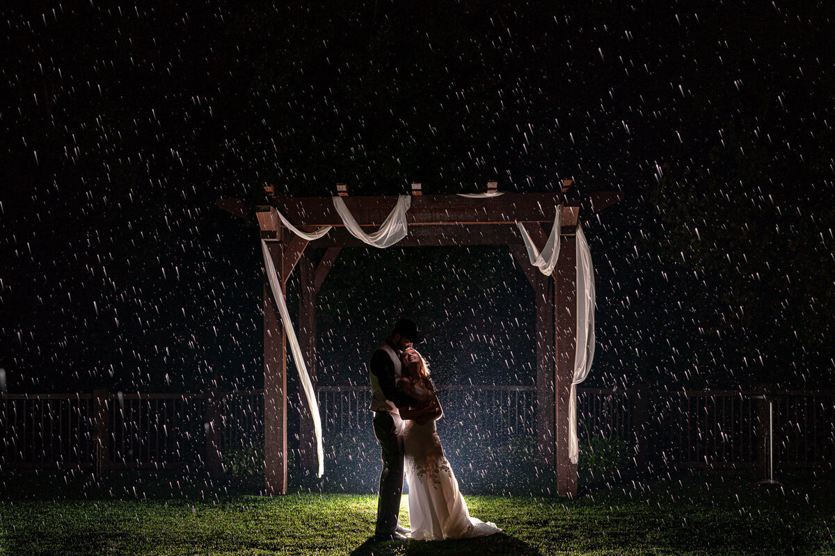 Bride and groom dance in the rain at night.